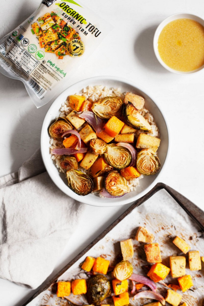 A sheet pan supper is pictured in the middle of assembly. Roasted vegetables have been transferred from a baking sheet to a small bowl, accompanied by a vinaigrette. 