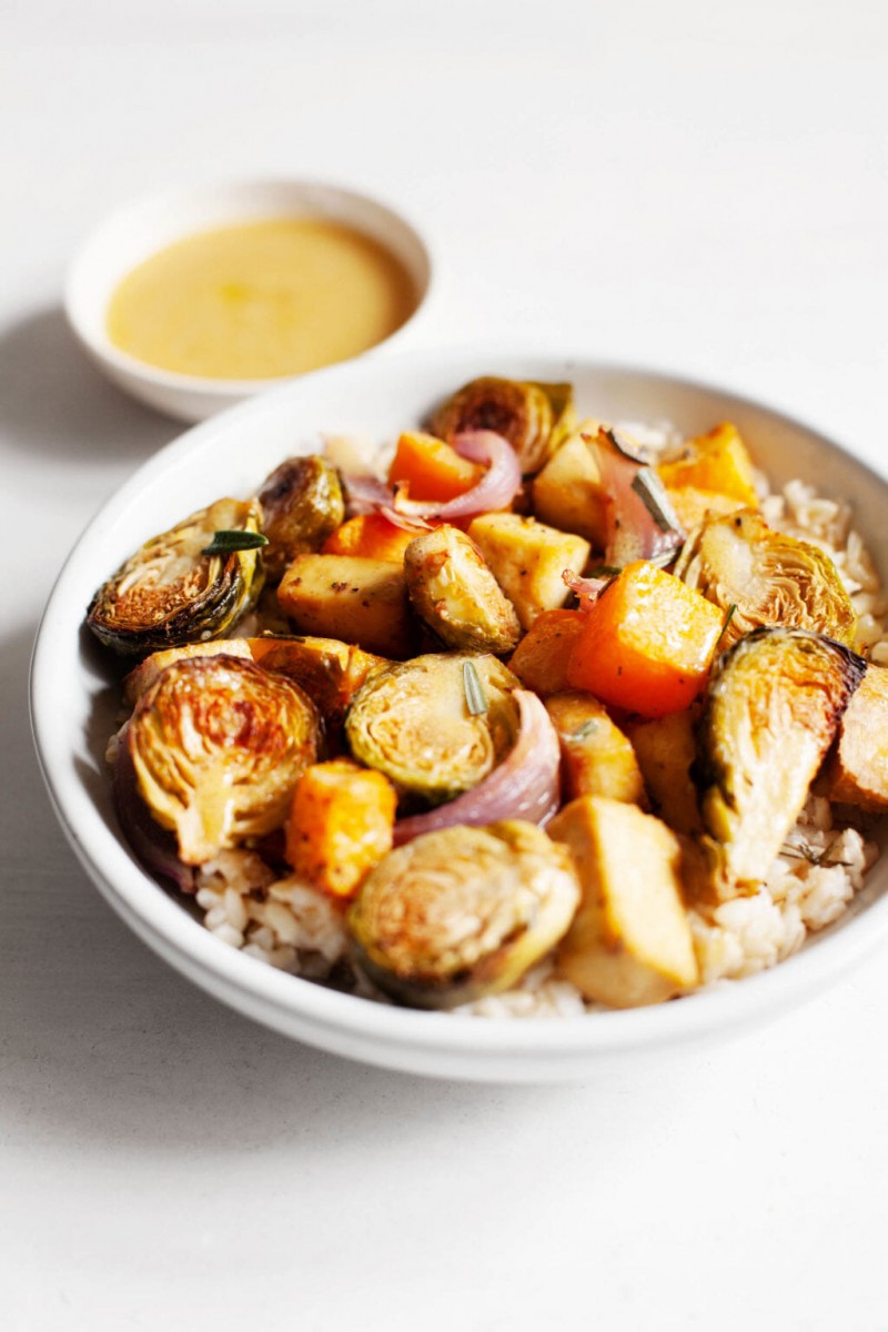 A serving bowl of seasonal, autumn produce is served over rice and accompanied by a small bowl of vinaigrette on the side.