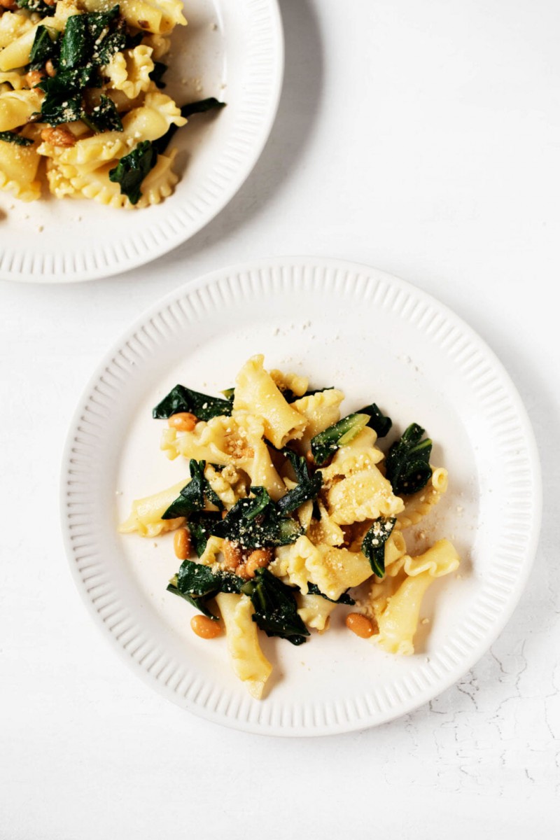 Two small serving plates with a plant-based dinner of cooked pasta, legumes, and vegetables.