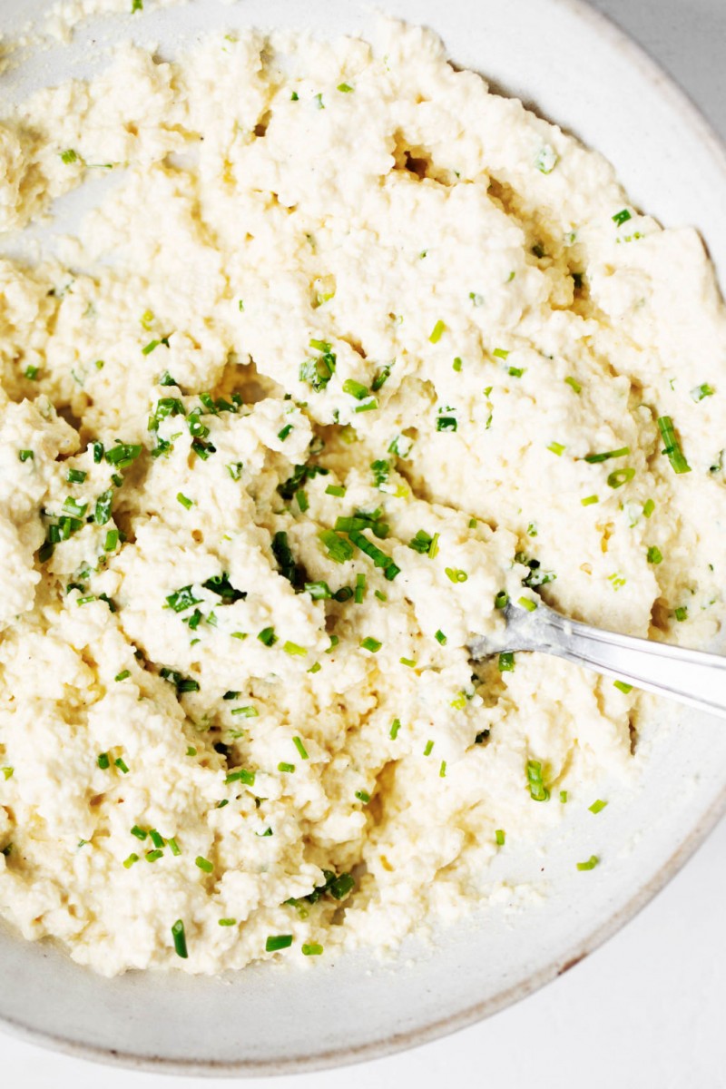 A bowl of a plant-based spread made with tofu. The tofu is topped with fresh herbs.