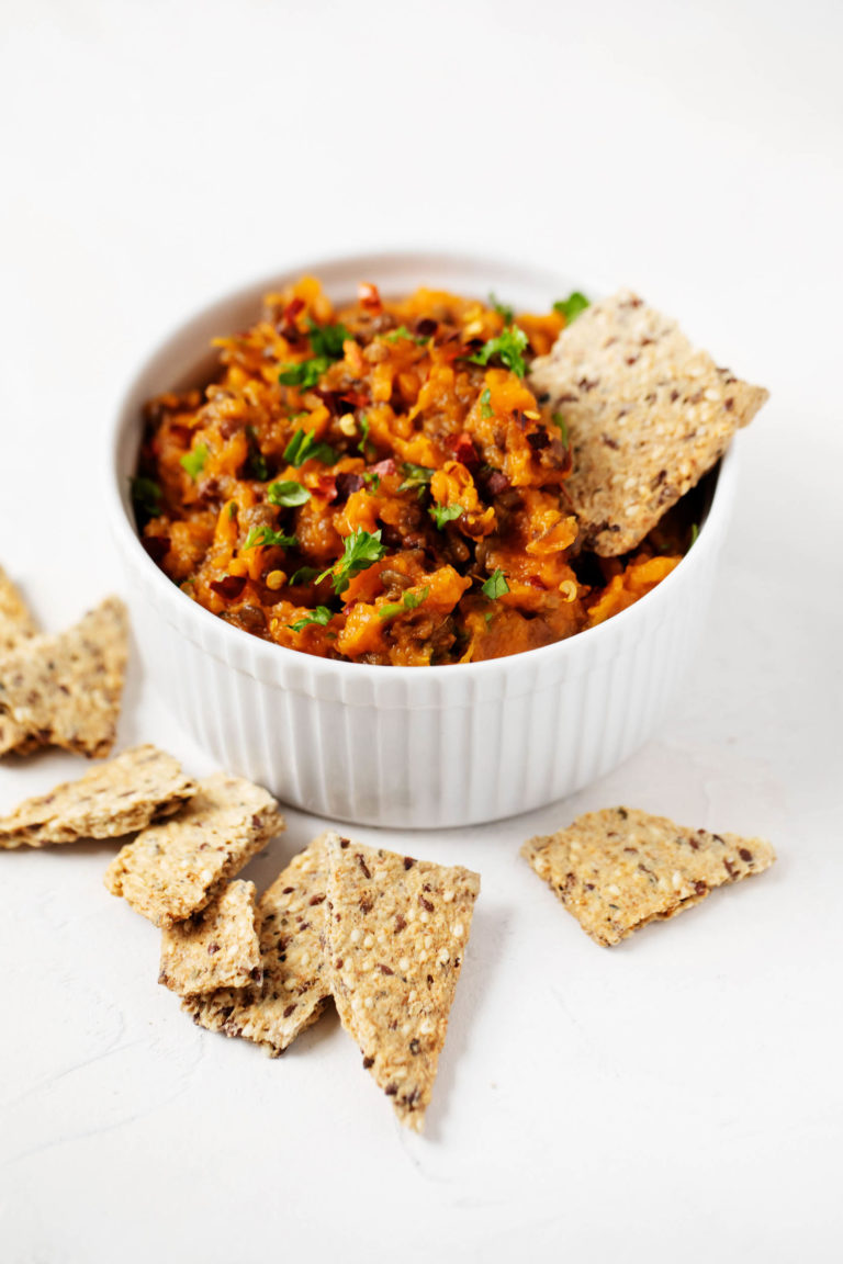 A white ramekin has been filled with a lentil sweet potato salad and is accompanied by crackers.