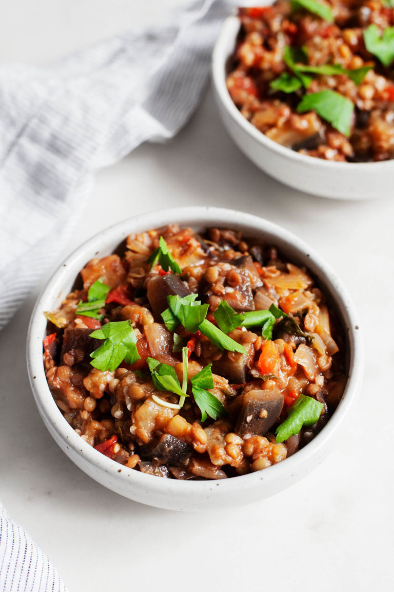 An image of stewed eggplant tomato lentils with fresh parsley on top.