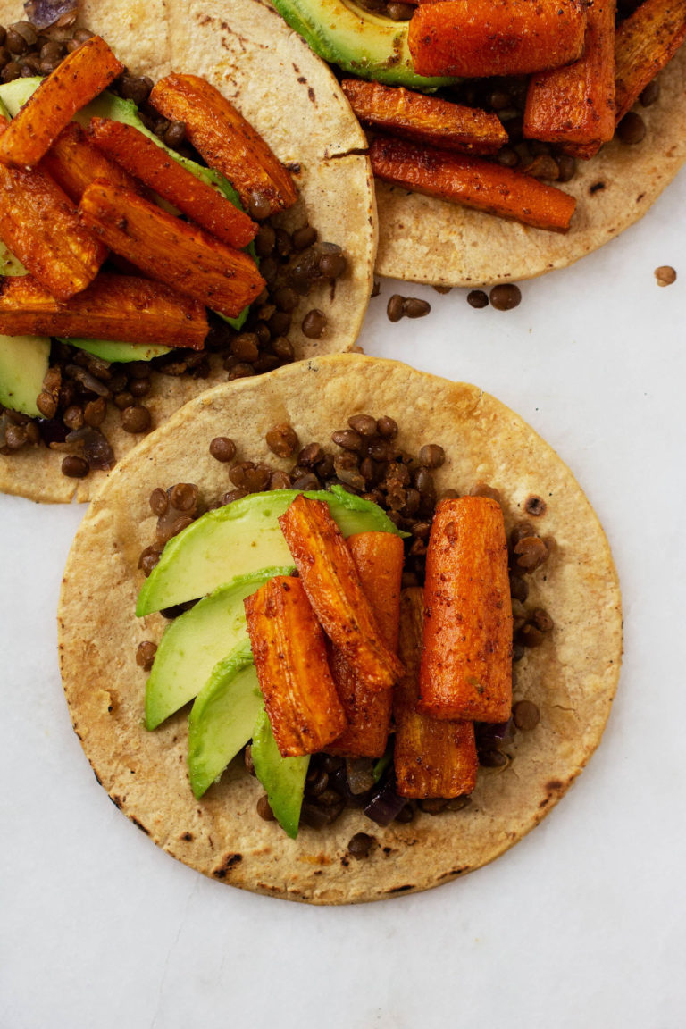 Three vegan roasted carrot lentil tacos with avocado slices.