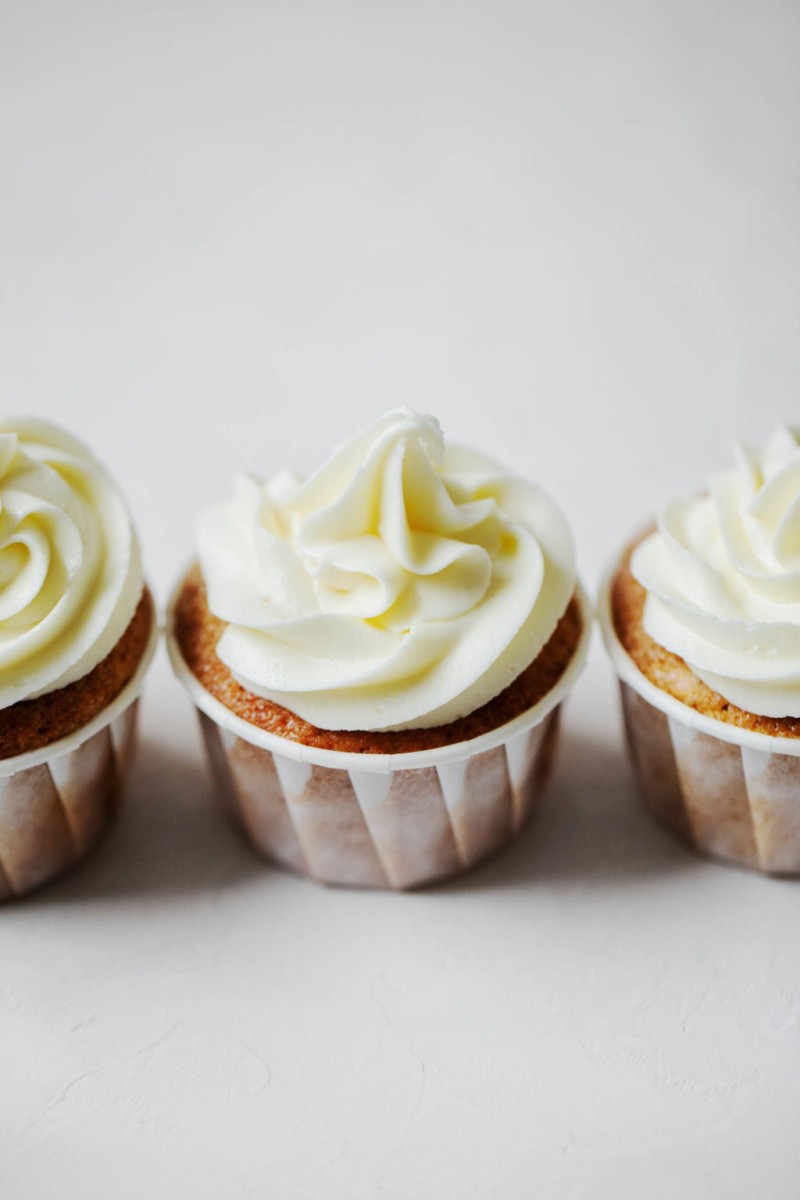 Three frosted vegan apple cider cupcakes, lined up in a row.