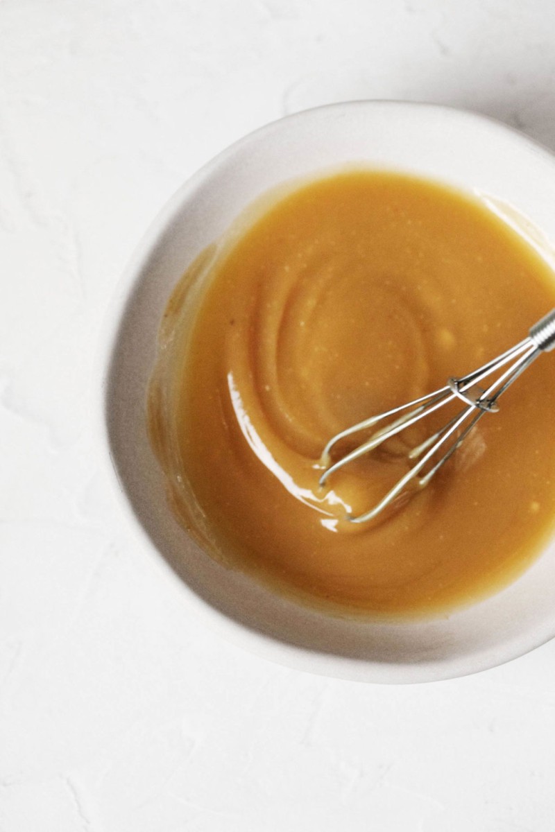 A small white pinch bowl is filled with a syrupy, amber colored glaze.