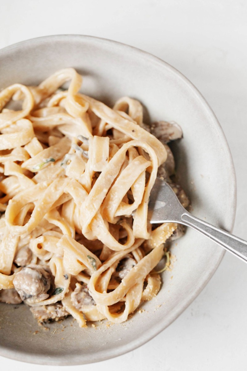 A creamy vegan mushroom pasta is being twirled on a fork. It rests in a round bowl.