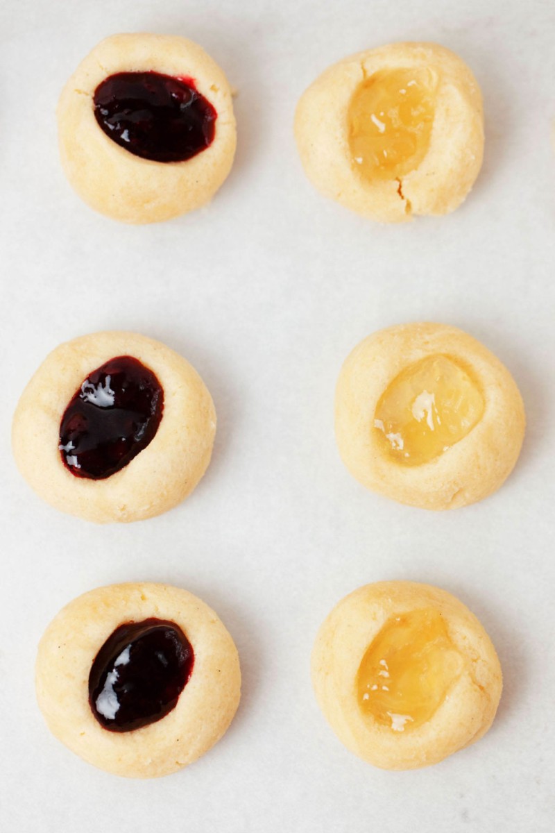 Balls of raw cookie dough have been indented and filled with jam. They rest on a parchment lined baking sheet.