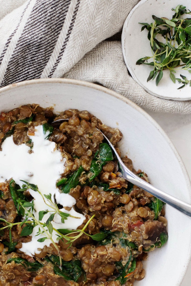 A close up, overhead image of grains and lentils with spinach that are smothered in white cashew cream.