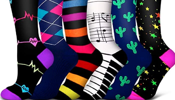 Six compression socks are shown against a white background. From left to right, there are designs including a heartbeat monitor, argyle, stripes, musical notes, cacti, and stars.