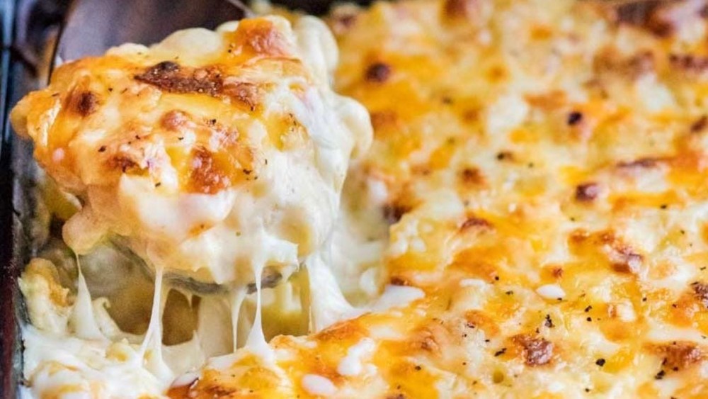 A forkful of baked macaroni and cheese being held over a casserole dish full of it. 