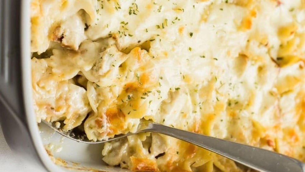 A casserole dish full of chicken alfredo bake and a spoon scooping some out. 