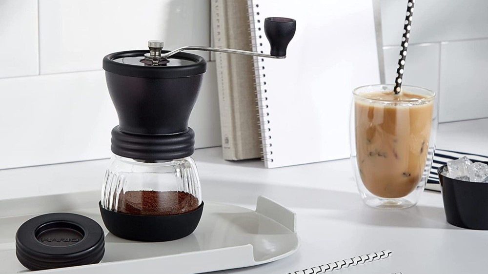 An image of the Hario ceramic mill placed over a plastic try with an iced coffee dirnk on the side.