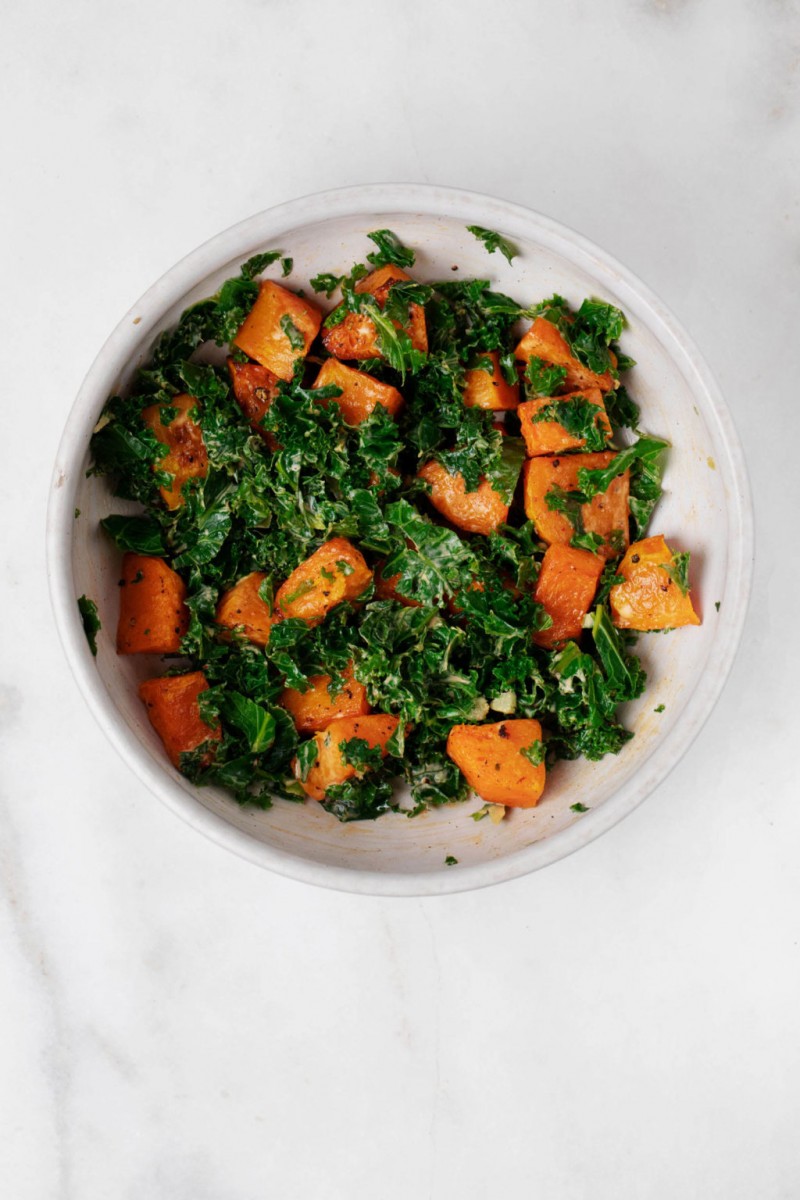 A white, ceramic bowl is filled with steamed kale and vegetables.