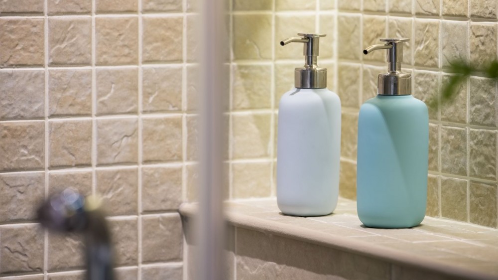 Two pump bottles of shampoo and conditioner in a shower.