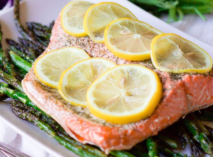 Steamed salmon topped with slices of fresh lemon and a bed of asparagus.