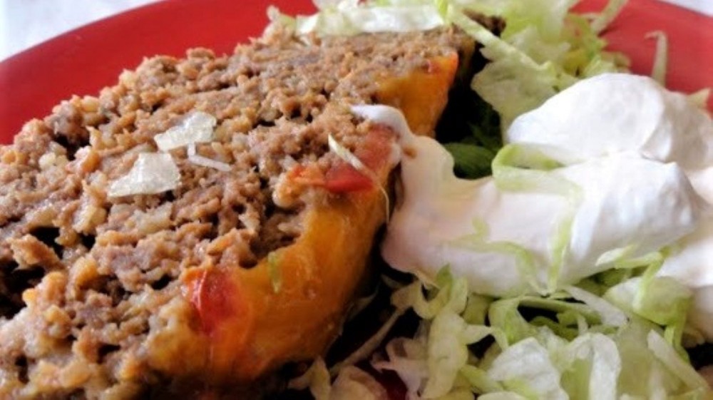 A slice of taco meatloaf on a plate next to some shredded lettuce topped with sour cream.