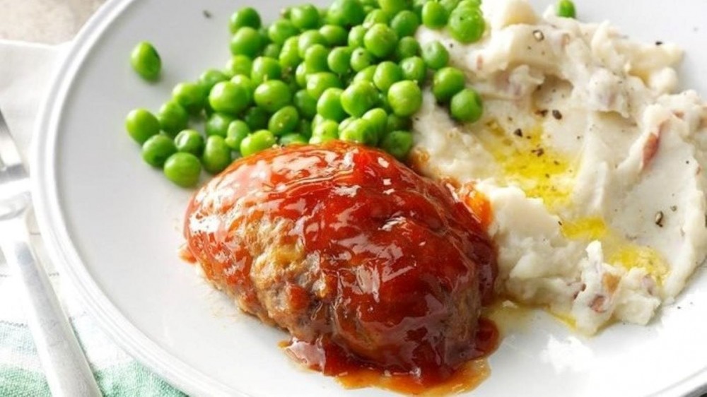 A Li'l Cheddar Meatloaf on a plate with mashed potatoes and peas. 