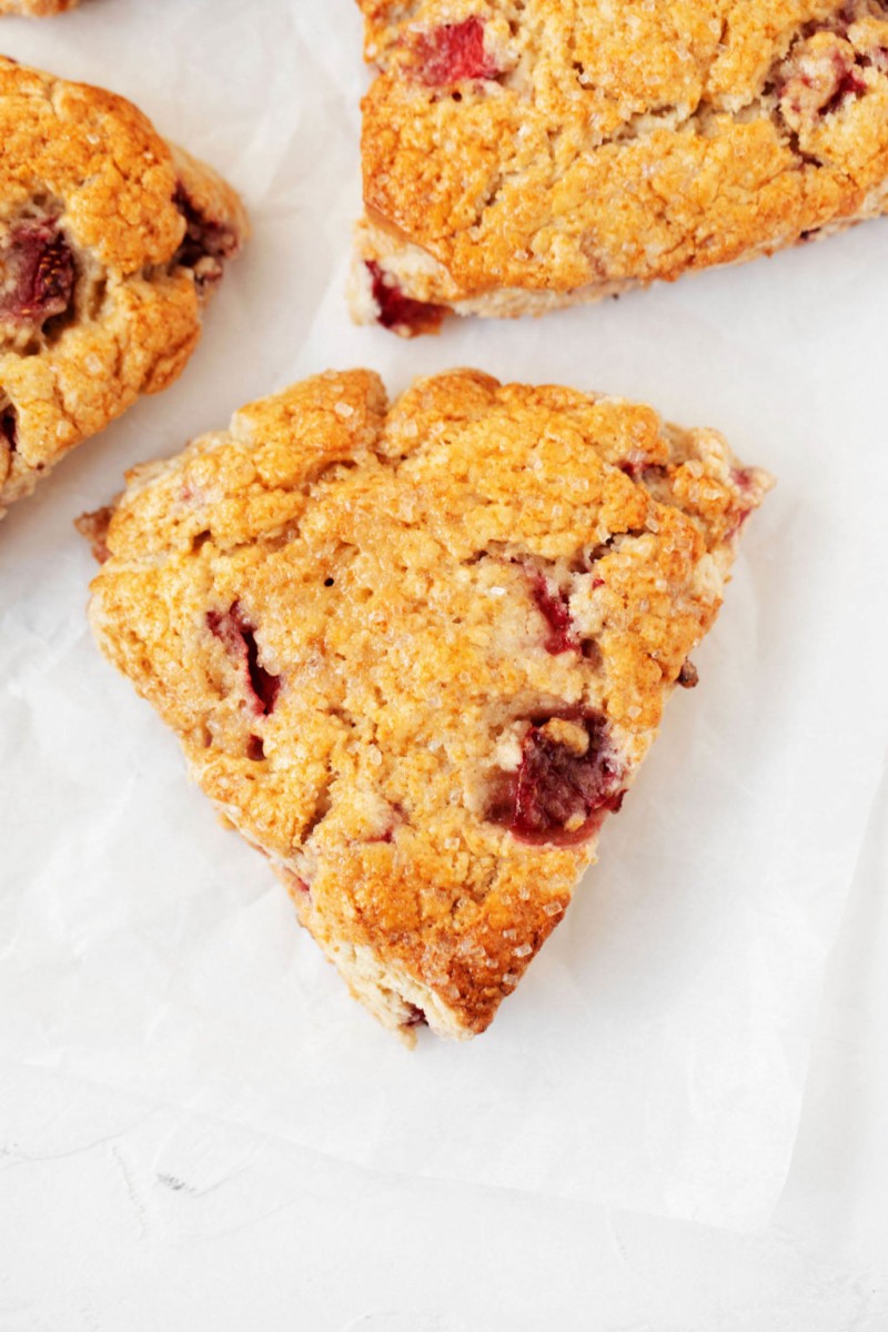 An overhead image of strawberry scones on a white parchment baking sheet.