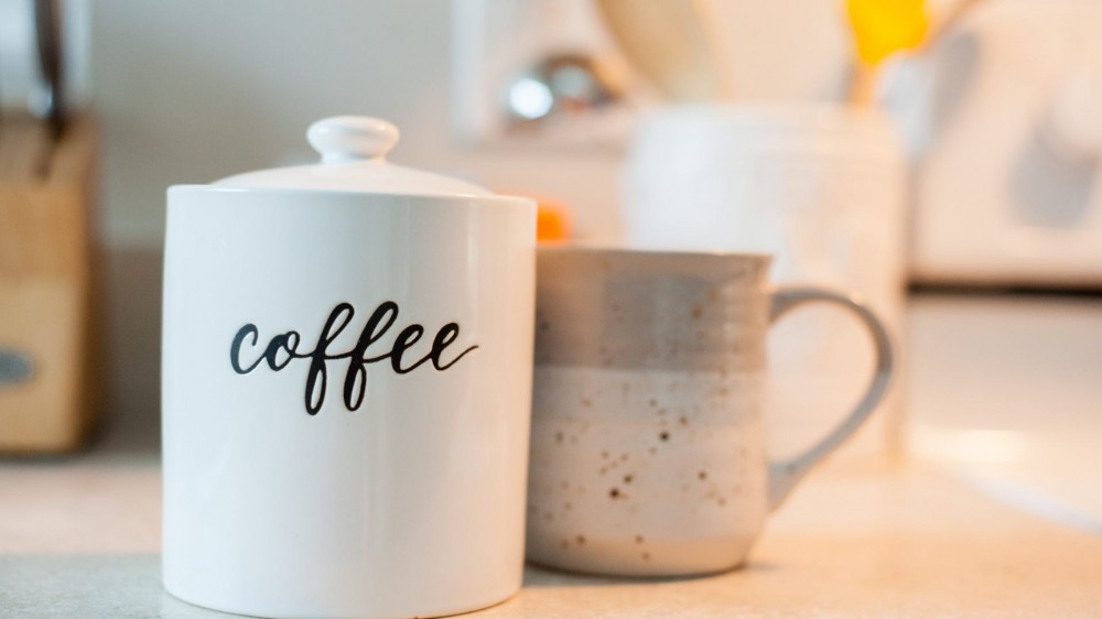 A white engraved coffee canister next to a coffee mug. 