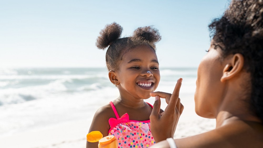 Young mother applying protective sunscreen on her daughter's nose at the beach.