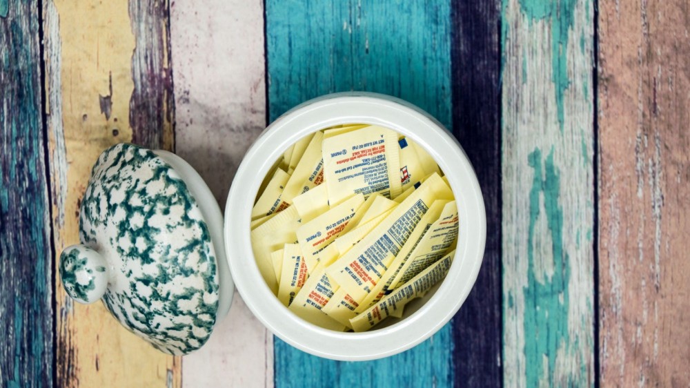 A jar of artificial sweetners on a wooden board.