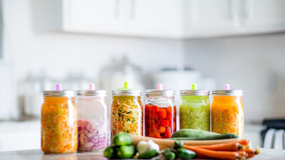 A variety of fermented vegetables in glass bottles on a kitchen counter.