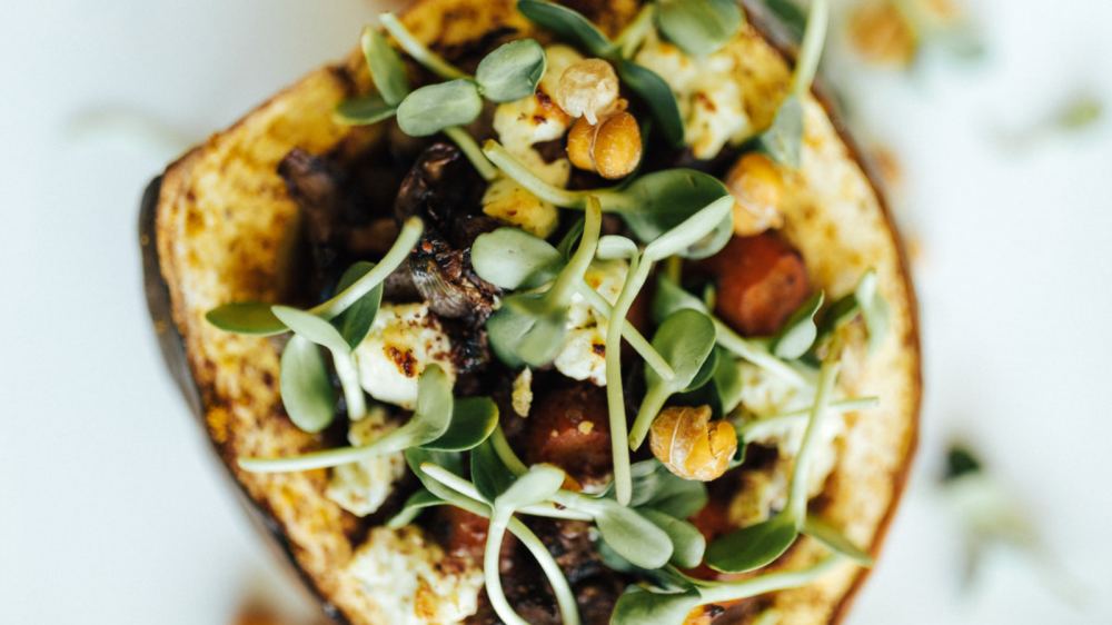 A close up of acorn squash filled with veggies, feta cheese, and chickpeas.