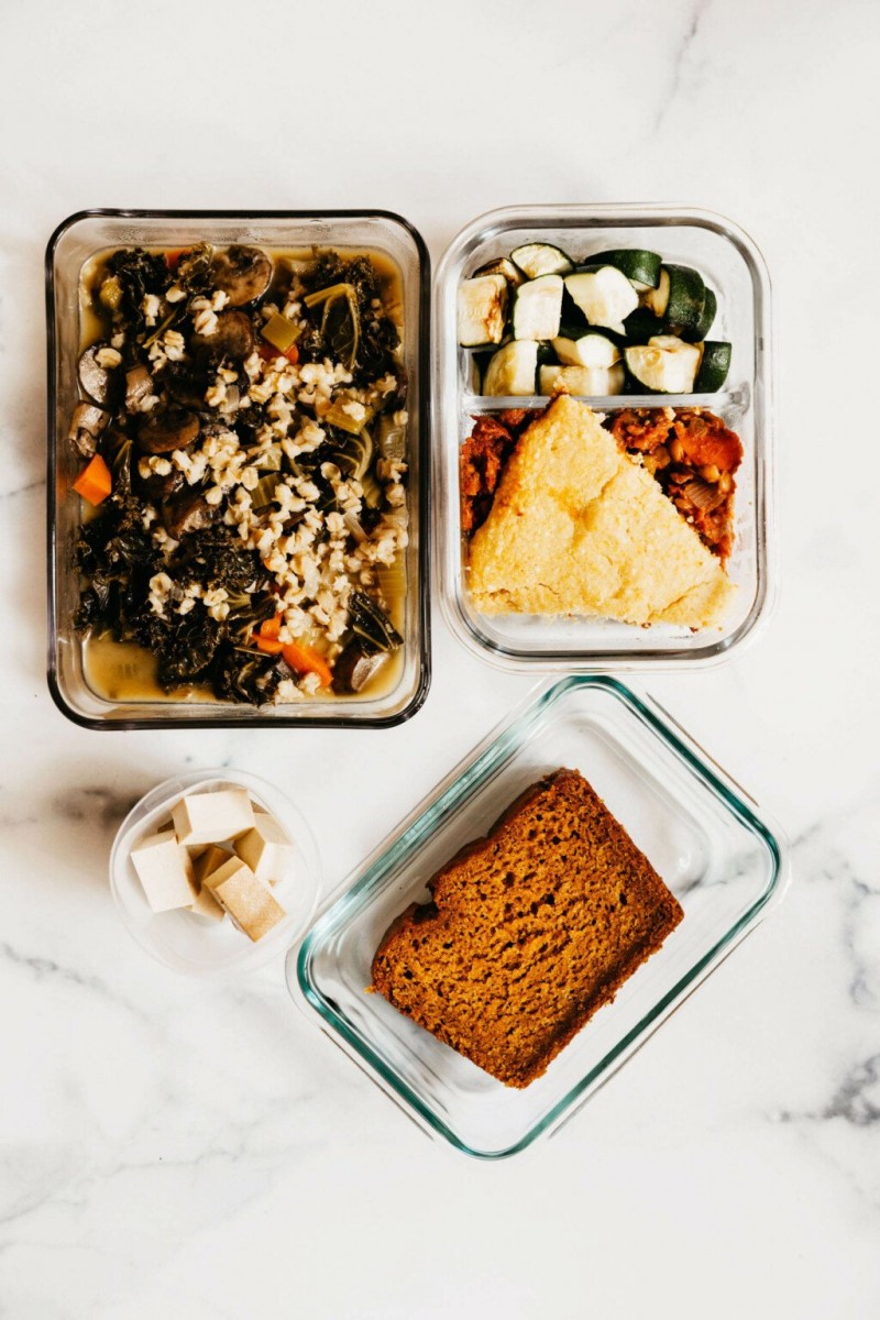 Various storage containers are resting on a white surface. They're filled with recipes that are part of a vegan meal prep.