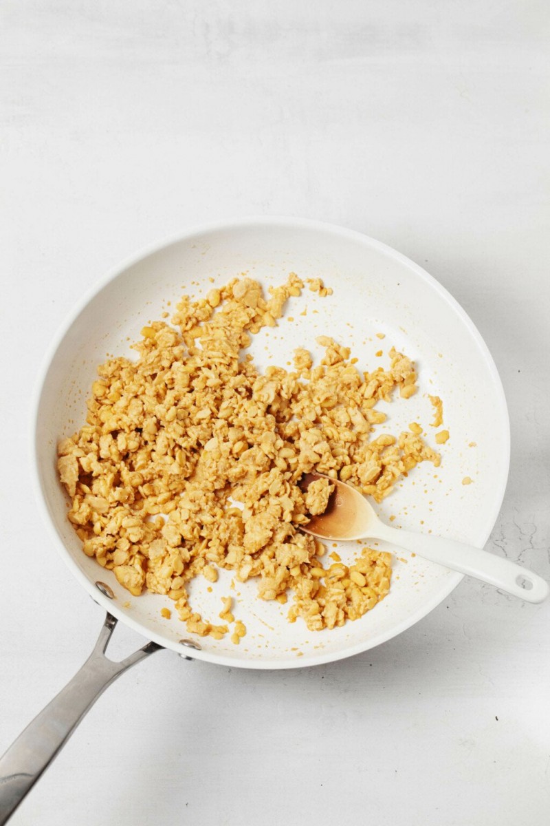 A small, white nonstick skillet is being used to cook crumbled tempeh.