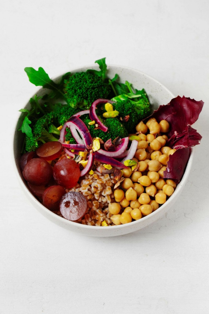 A colorful bowl with chickpeas, vegetables, and pickled onions is resting on a white surface.