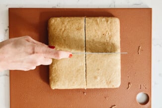 A single sheet of square vanilla cake is being cut into four squares.