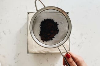 A square dish of tiramisu is being dusted with cocoa powder.