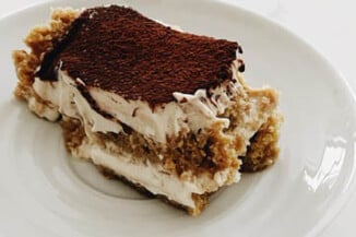 A creamy slice of vegan tiramisu is resting on a small white plate.