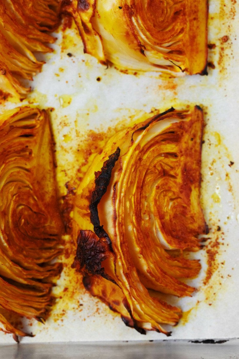 Freshly roasted cabbage steak wedges are laid out on a baking sheet, with parchment beneath them.