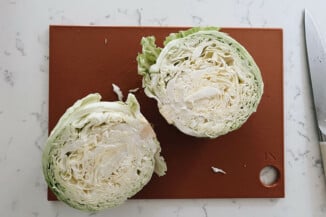 A large head of cabbage has been cut in half on a cutting board.