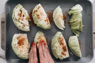 Cut wedges of cabbage are being basted with a spice rub.