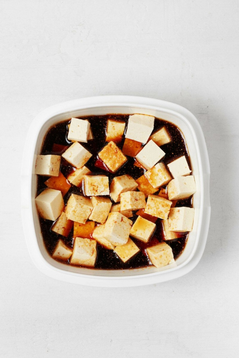 Cubes of tofu are marinating in darkly colored soy sauce and other seasonings.