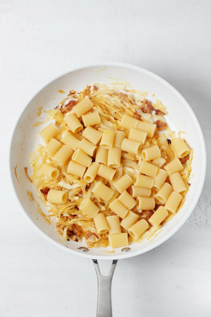 Cooked pasta has just been added to a skillet with sautéed vegetables.