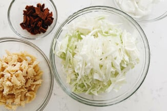 Vegetables have been prepared for a pasta recipe. They're laid out in clear bowls on a white surface.