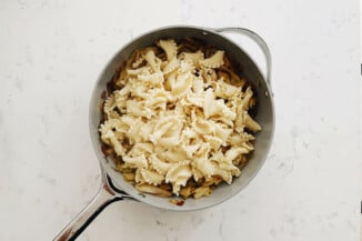 Cooked pasta has just been added to a skillet with sautéed vegetables.