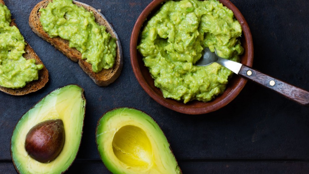 Sliced up avocados and guacamole on a table.