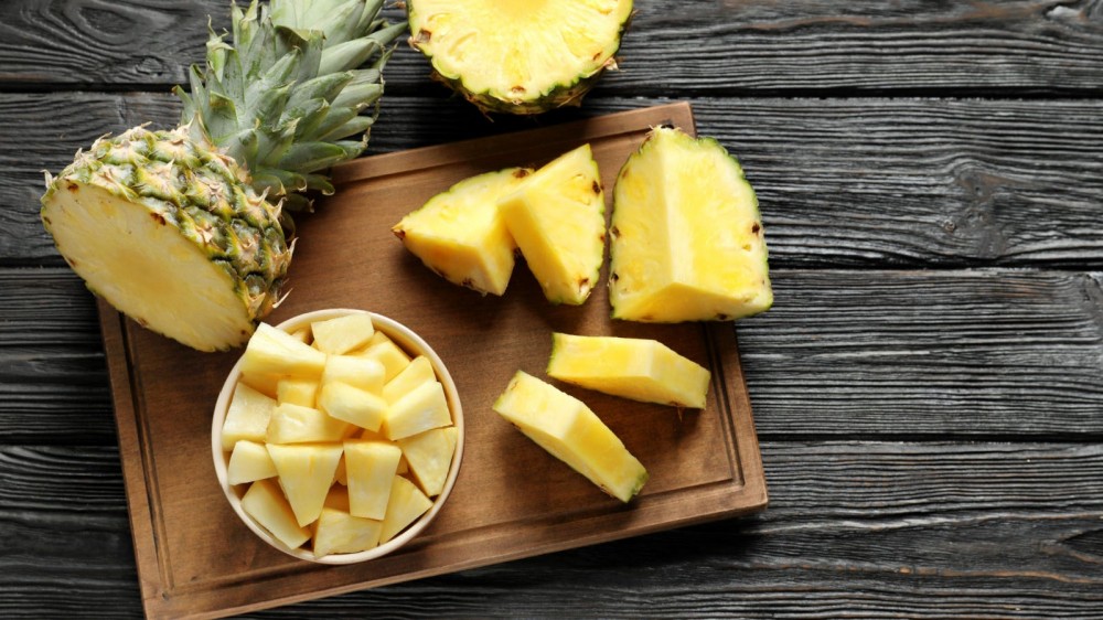 Pineapple cut in slices and cubes on a wooden board.