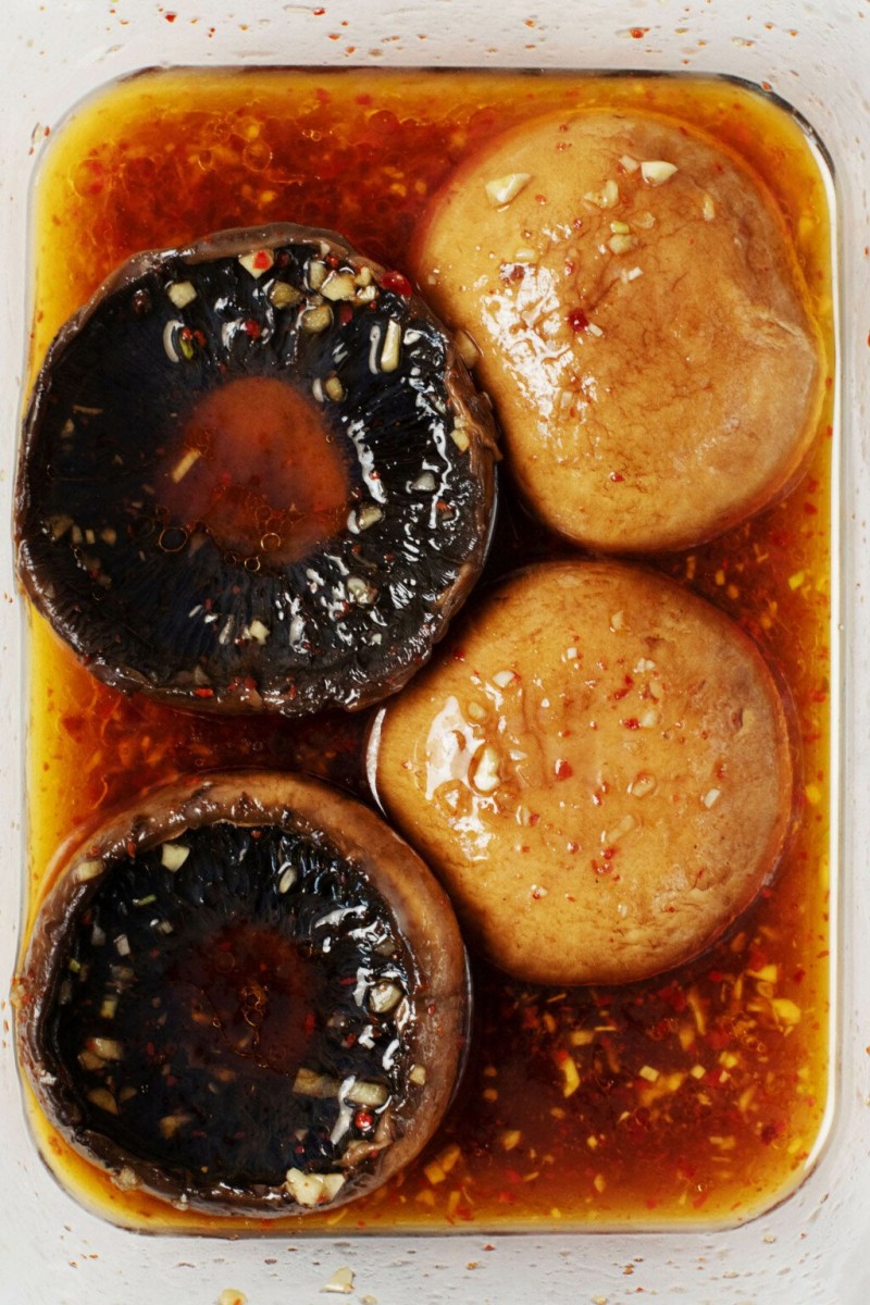 A large, glass storage container is being used to marinate mushroom caps.