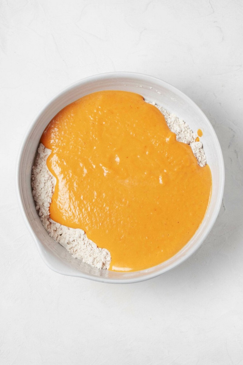 A large, white mixing bowl is pictured overhead. It contains flour and a wet mixture of ingredients, which will soon be mixed with the flour.