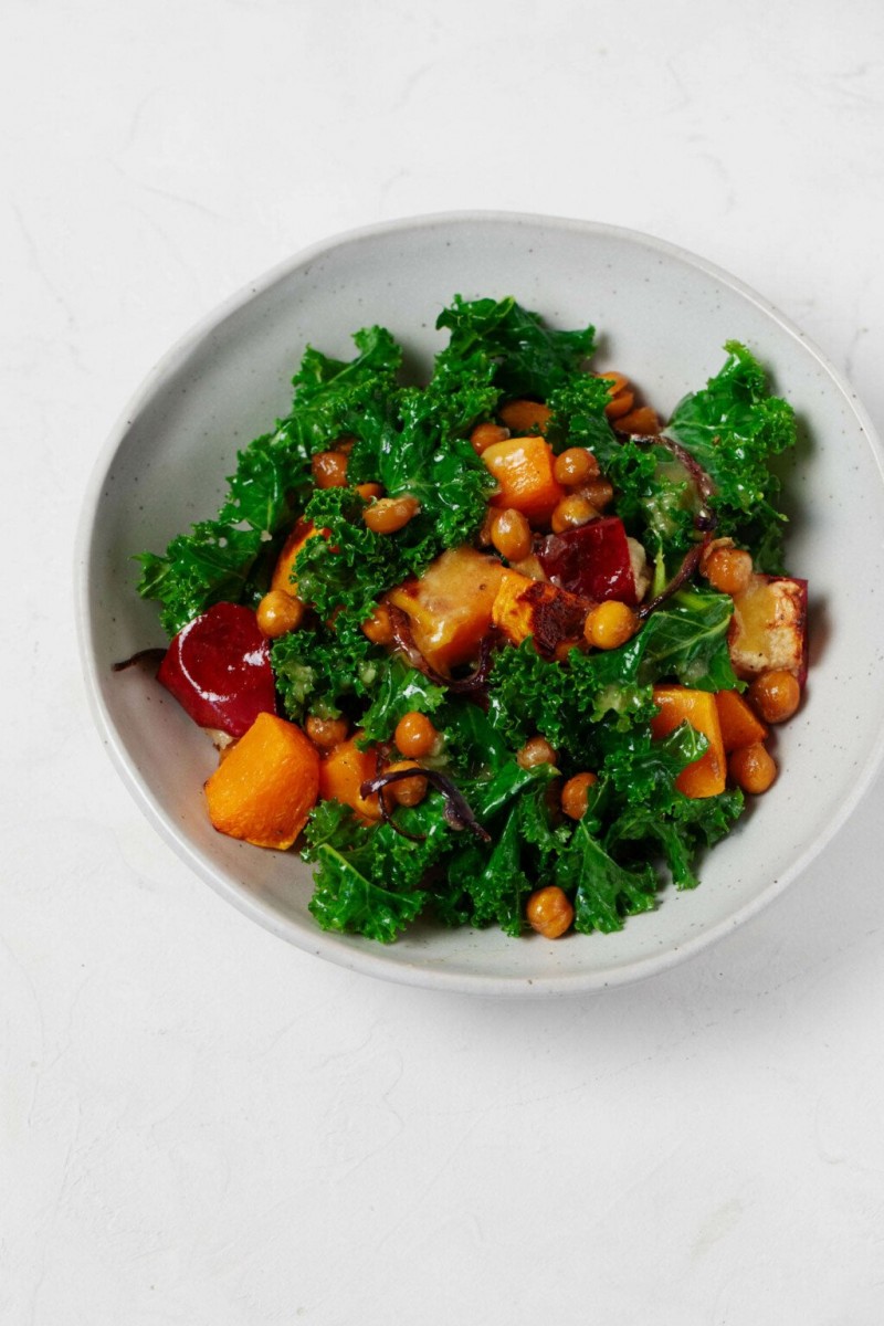 An overhead image of a white bowl, which is filled with kale, squash, and other ingredients.