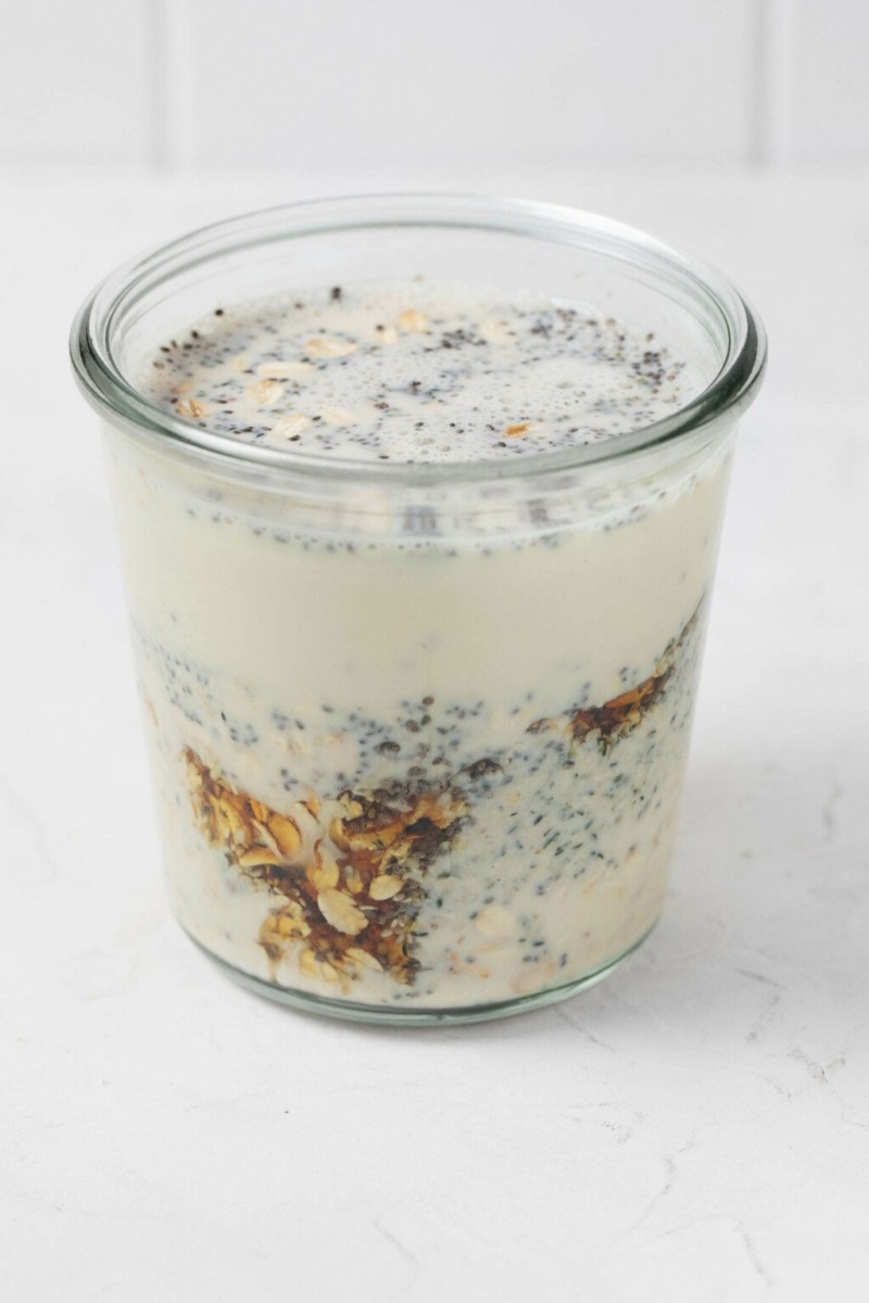 A mason jar is being used to mix and store overnight oats. It rests on a white surface.