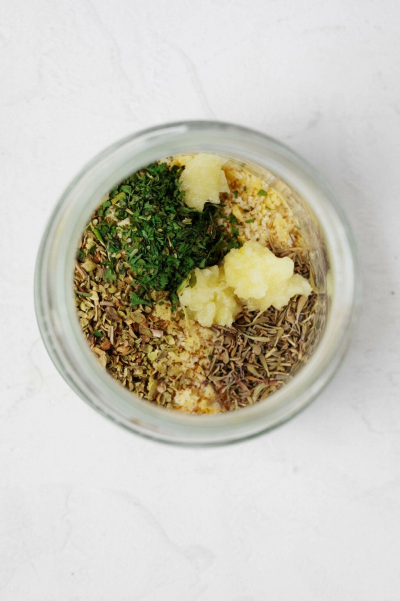 An overhead image of a glass jar, which contains herbs and garlic.