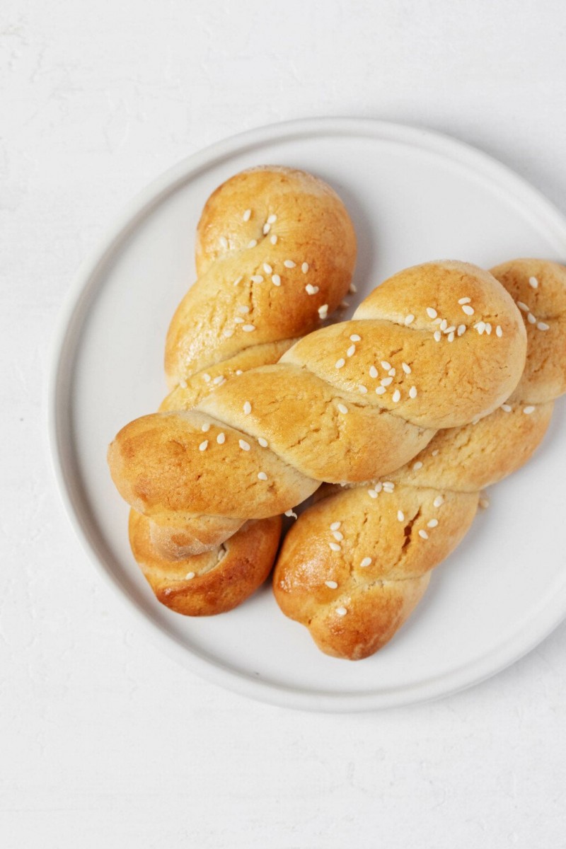 An overhead image of a small, round, rimmed white plate, which is topped with braided koulourakia cookies.