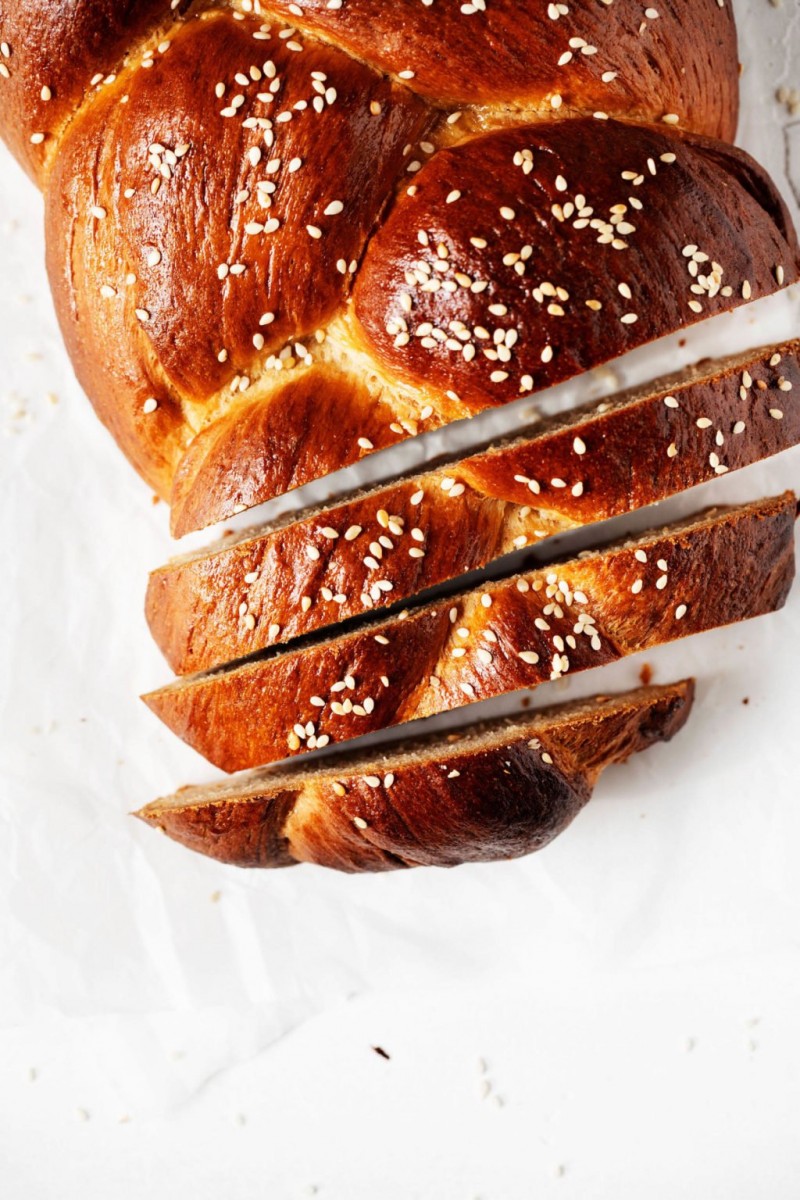 An overhead image of a braided vegan Tsoureki sweet bread, which has been sliced on top of white parchment paper.